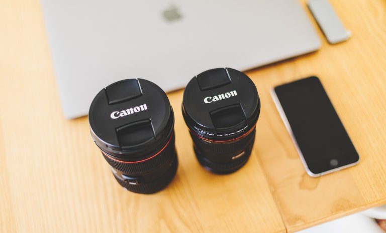 photo focused on two canon camera lenses on a table with an apple laptop and iphone in the background