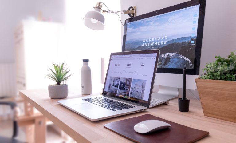 wooden desk with laptop and desktop with inspirational wallpaper and neutral colored décor