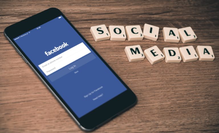 phone screen displaying a Facebook log-in screen with the words "social media" spelled out in Scrabble letters