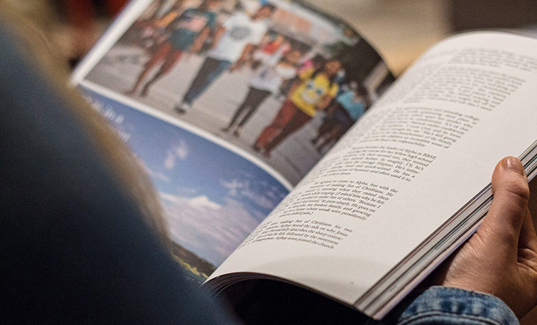 person holding an open magazine with an advertisement and photos on the left page and a story on the right page