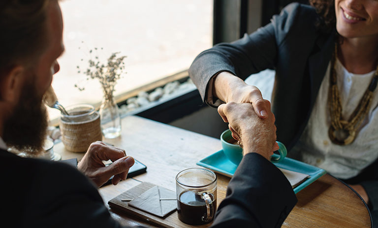 photo of a man and woman at a table exchanging a handshake over tea and coffee