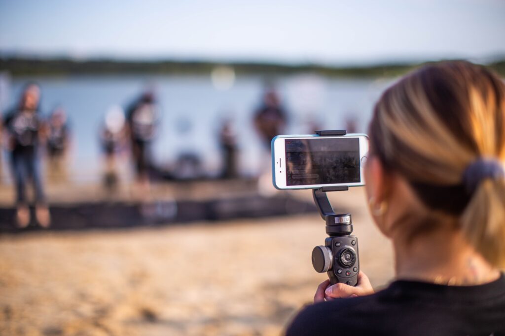 woman holding a black gimbal stabilizer filming an adult yoga on the beach with a white iPhone