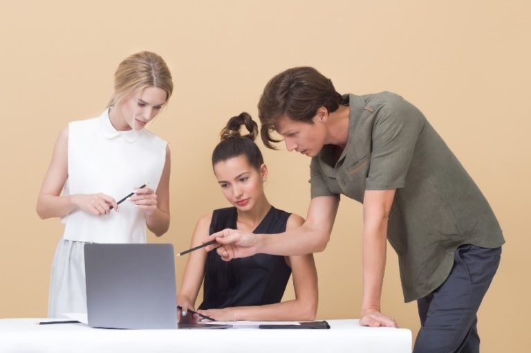 Two women and a man looking at a laptop critiquing the work