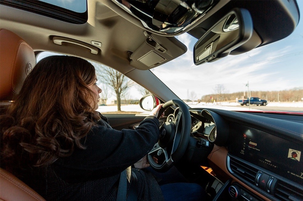 woman with brown curly hair wearing a black jacket sitting in a 2019 Alfa Romeo Giulia with two-tone brown and black leather car interior