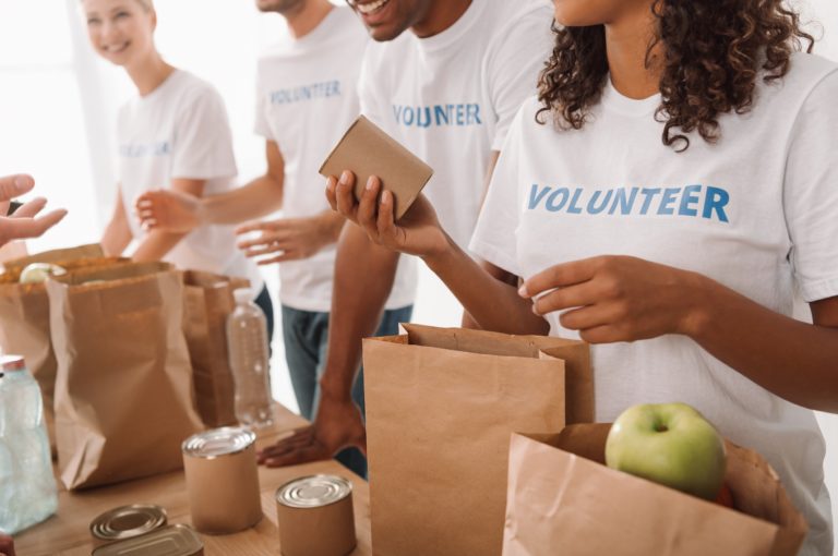 group of adults wearing white shirts with blue volunteer lettering bagging groceries for charity