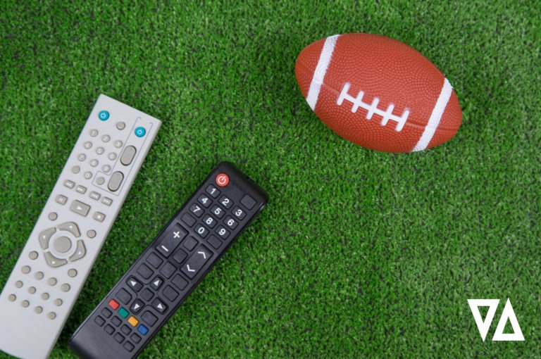 gray and black television remotes placed on green turf close to a brown football with white laces and stripes