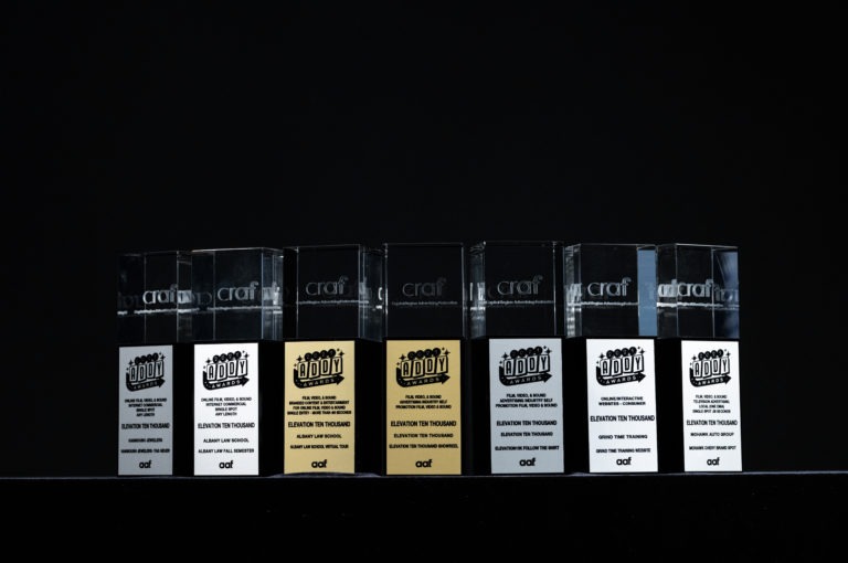 five silver and two gold Capital Region American Advertising Awards trophies on a black stand in front of a black background