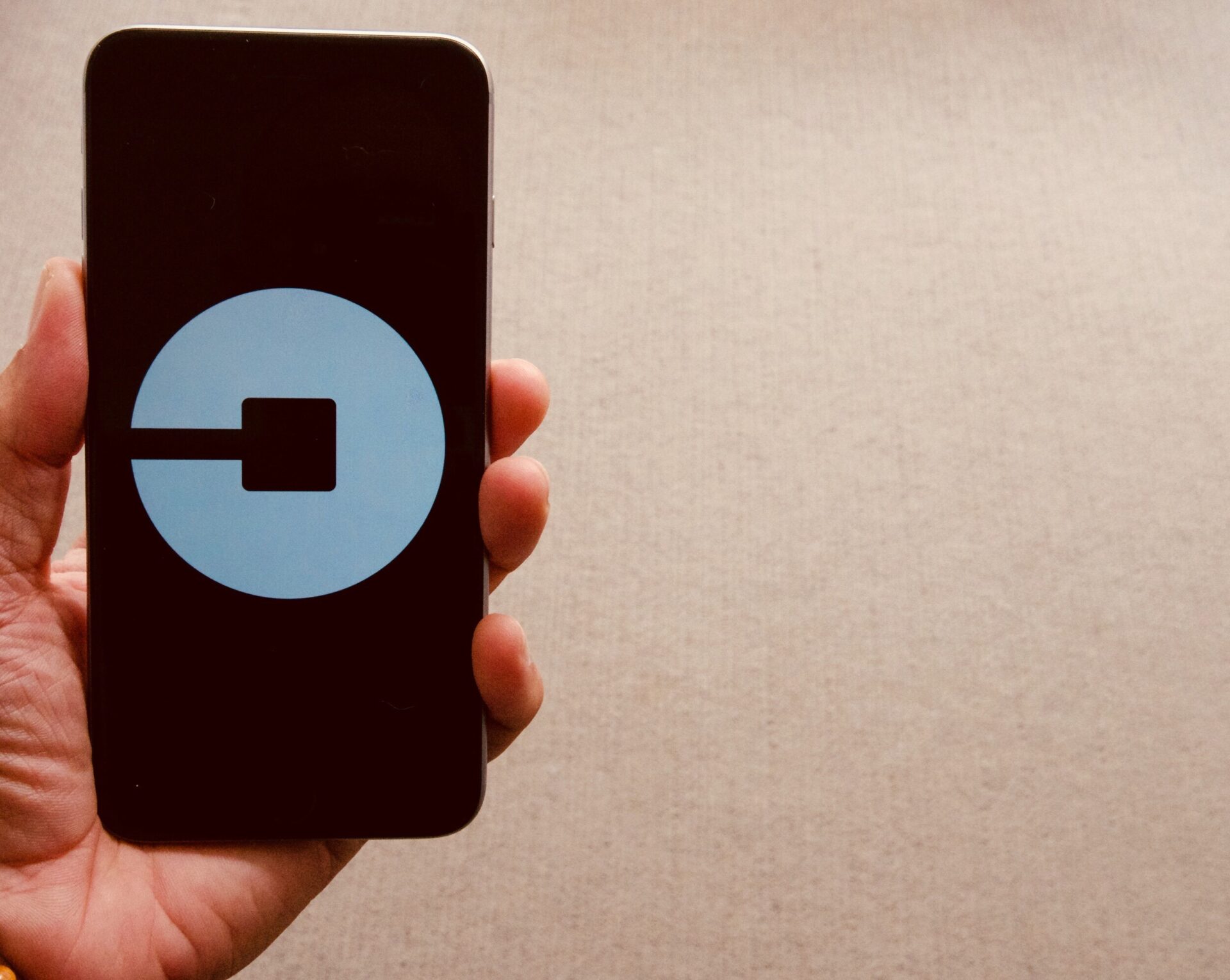 closeup of person’s hand holding a black iPhone displaying the rebranded Uber logo, a white circle against black background