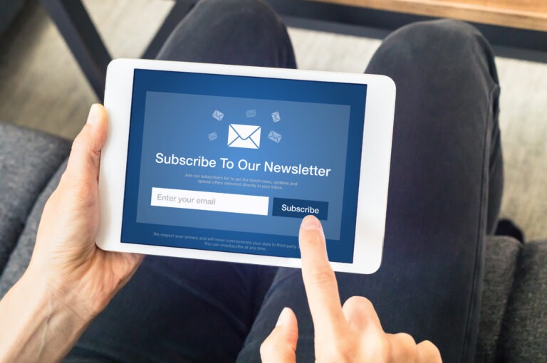 adult wearing black pants and holding a white tablet showing a blue screen encouraging users to subscribe to an email marketing newsletter
