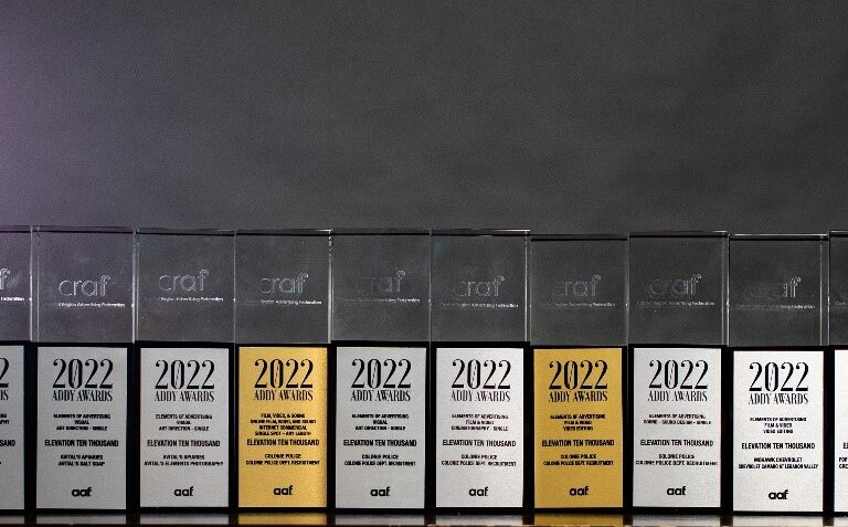14 glass trophies for content marketing with silver and gold plaques lined in front of a gray backdrop