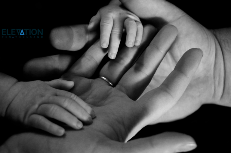 black and white photo of two baby hands on top of two adult hands