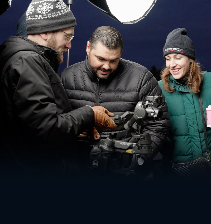 Thumbnail of three people looking at a video camera on the set of a shoot